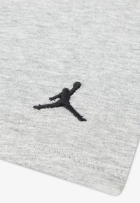 Tissu en coton gris avec une finition texturée présentant un logo Jumpman brodé en noir. Coutures visibles le long du bord.
