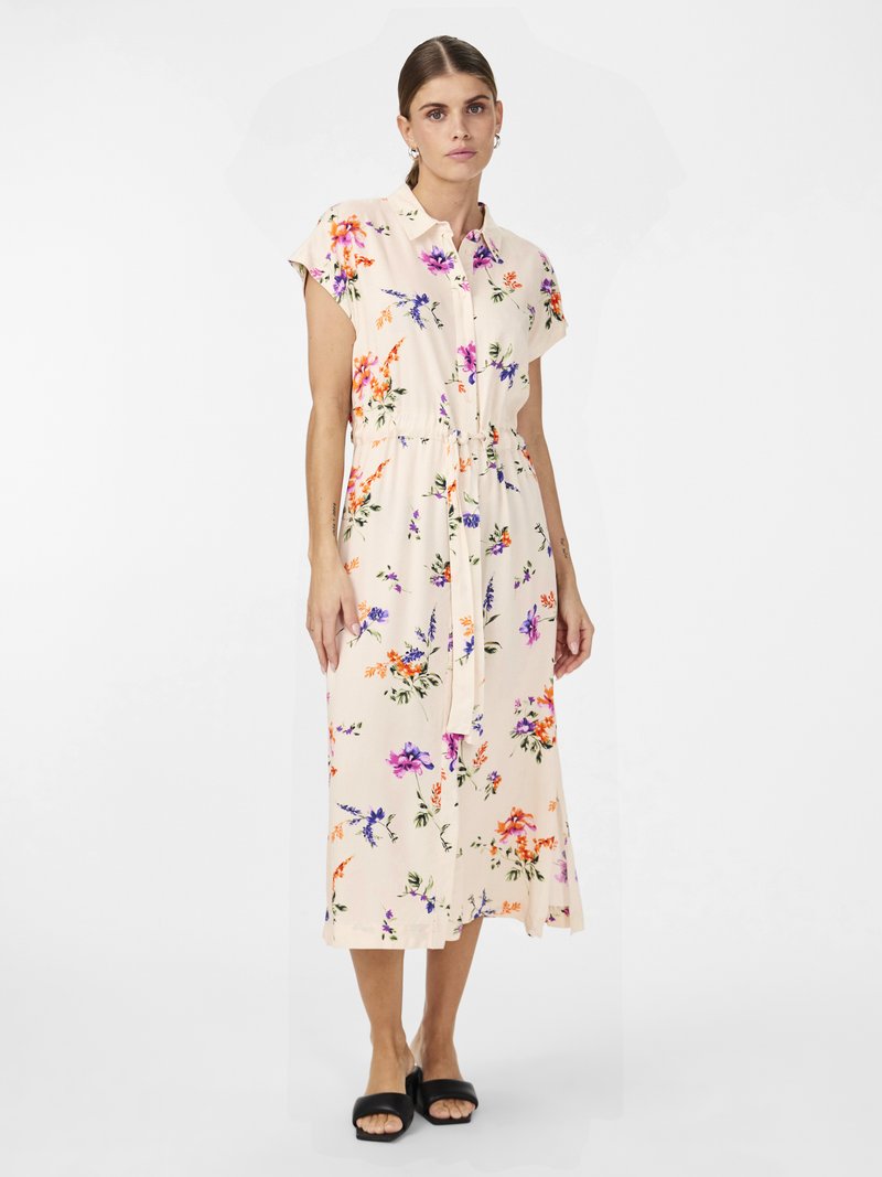 Robe midi florale en crème, avec col, manches courtes, taille cintrée et divers motifs de fleurs colorées. Sandales à glissière noires.