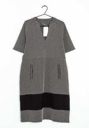 Schwarz-weißes kurzärmeliges Kleid mit kleinem geometrischem Muster, Brusttaschen, einem schwarzen horizontalen Streifen nahe dem Saum, hängend an einem schwarzen Kleiderbügel.