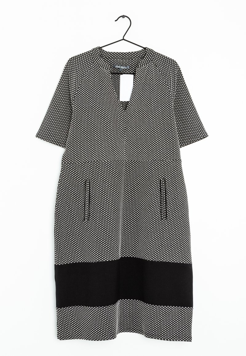 Robe manches courtes noir et blanc avec un petit motif géométrique, poches poitrine, une bande horizontale noire près de l'ourlet, suspendue sur un cintre noir.