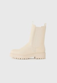 Beige ankelboots med en glatt skinntekstur, chunky såle, elastiske sidestykker og en pull-tab; har merkevarelogo på siden.