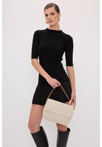 Zwarte geribbelde top met korte mouwen en een aansluitende silhouet, gecombineerd met een zwarte geplooide minirok. Draagt een beige handtas met een gouden ketting.