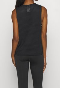 Svart ärmlös atletisk topp med ett strukturerat mönster, rund halsringning och en liten nätdetalj på baksidan, i kombination med svarta leggings.