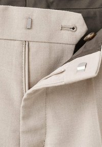 Tessuto beige con una trama diagonale, caratterizzato da una vita grigia, chiusure metalliche e una chiusura con bottone. Include un dettaglio con asola cucita.
