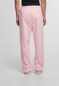 Light pink sweatpants with a relaxed fit, featuring an elastic waistband and side seams. Made of soft, textured fabric suitable for casual wear.
