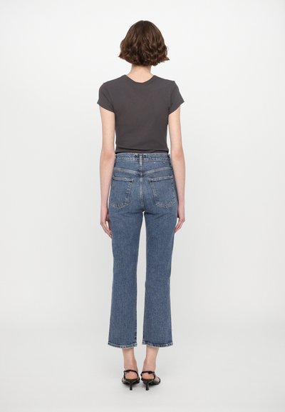 Grå t-shirt med kort ärm i kombination med högmidjade, rakbeniga blå jeans. Jeansen har bakfickor och en rå fåll.