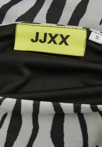 Tkanina sa uzorkom zebre s crno-bijelim prugama, sadrži žutu oznaku na kojoj piše "JJXX" i veličinu "S" na crnoj pozadini.