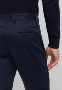 Námořnické modré chino kalhoty vyrobené z hladkého materiálu, s zadní kapsou s jemnou štítkem loga a poutkem na opasek v pase.