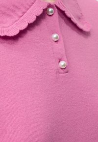Tissu tricoté rose avec trois boutons en nacre et un bord de col côtelé et froncé.