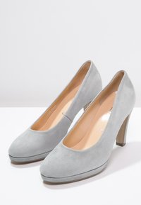 Escarpins en suede gris avec un bout arrondi, un talon de 10 cm et une plateforme subtile. Texture lisse avec une finition naturelle.