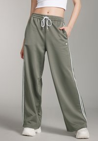 Olivgrüne, weit geschnittene Sweatpants aus glattem Stoff, mit wei�ßen Seitenstreifen, elastischem Bund und Zugband sowie seitlichen Taschen.