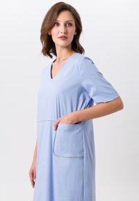 Helles blaues Kleid mit V-Ausschnitt, kurzen Ärmeln und einer Tasche. Hergestellt aus weichem Stoff mit sichtbaren Nähten entlang der Tasche.