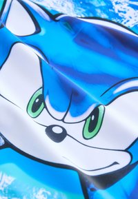 Blåt stof med et stiliseret tegneseriefigur med store grønne øjne, en hvid snude og sorte accenter på en vandinspireret baggrund.