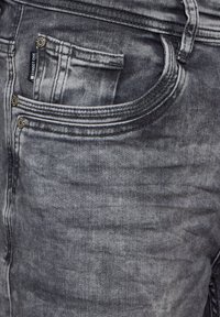 Jeans de mezclilla gris con una textura desgastada, costuras visibles y bolsillos frontales. Incluye una pequeña etiqueta de marca cerca del bolsillo izquierdo.