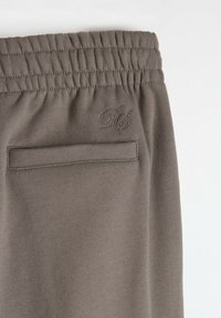 Szare dresy z prążkowanym paskiem w talii, z tylną kieszenią i subtelnym haftowanym logo. Gładka tekstura materiału.