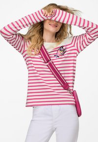 Camicia a maniche lunghe a righe rosa e bianca con una grafica di pesce; abbinata a una borsa a tracolla rosa con una tracolla texturizzata e dettagli in metallo.