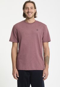 Camiseta color burdeos, de cuello redondo, manga corta, fabricada en una mezcla de algodón, con un pequeño logo negro en el lado izquierdo del pecho, textura suave.