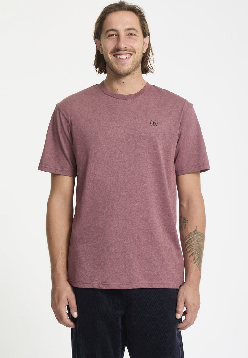 Camiseta color burdeos, de cuello redondo, manga corta, fabricada en una mezcla de algodón, con un pequeño logo negro en el lado izquierdo del pecho, textura suave.