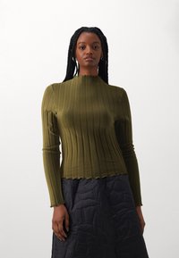 Oliven grønn ribbet topp med lange ermer og høy bølget halslinje, kombinert med et svart quiltet skjørt. Glatt tekstur, tettsittende design.