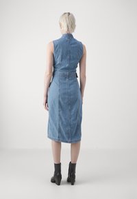 Abito di jeans con design senza maniche, vita aderente e gonna di lunghezza al ginocchio. Tessuto azzurro chiaro, cuciture verticali e cintura in jeans abbinata.