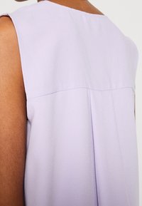 Haut sans manches violet en tissu léger, présentant une texture lisse, un design simple et un léger pli le long de la couture arrière.
