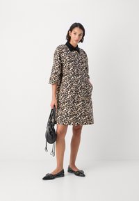 Haljina s uzorkom leopard, crnim ovratnikom, kratkim rukavima i džepovima, uparena s crnim ravnim cipelama i malom crnom torbicom.