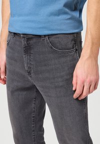 Vaqueros de mezclilla grises con un corte ajustado, que cuentan con bolsillos frontales, tejido texturizado y una cintura estándar. Combinados con una camiseta de algodón azul.