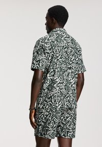Set di camicia a maniche corte e pantaloni shorts con un motivo astratto verde e bianco, realizzato in tessuto leggero con una vestibilità rilassata.
