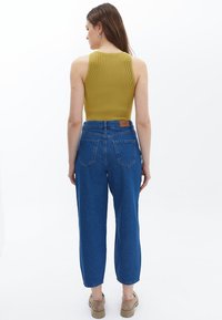 Top de tirantes acanalado en color oliva combinado con jeans de cintura alta azul; presenta un corte holgado y tobillos con dobladillo. Unos zapatos beige completan el conjunto.