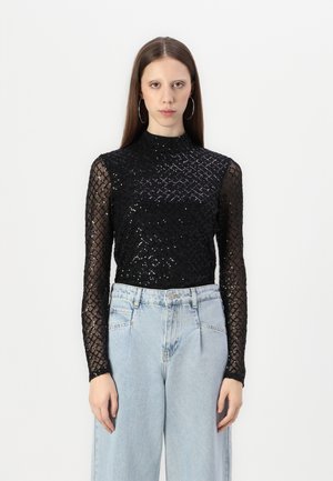 Black long-sleeve top with a high neck, made of sheer fabric and adorned with sequins in a diamond pattern, paired with light blue high-waisted jeans.