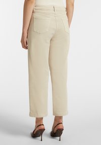 Pantaloni beige a gamba larga con vita alta, dotati di due tasche posteriori e una texture liscia. Abbinati a scarpe con tacco alto marroni.