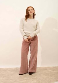 Jasnoszary, fakturowany sweter z długim rękawem połączony z szerokimi, różowymi spodniami z korduroju. Błyszczące czarne buty dopełniają całość.