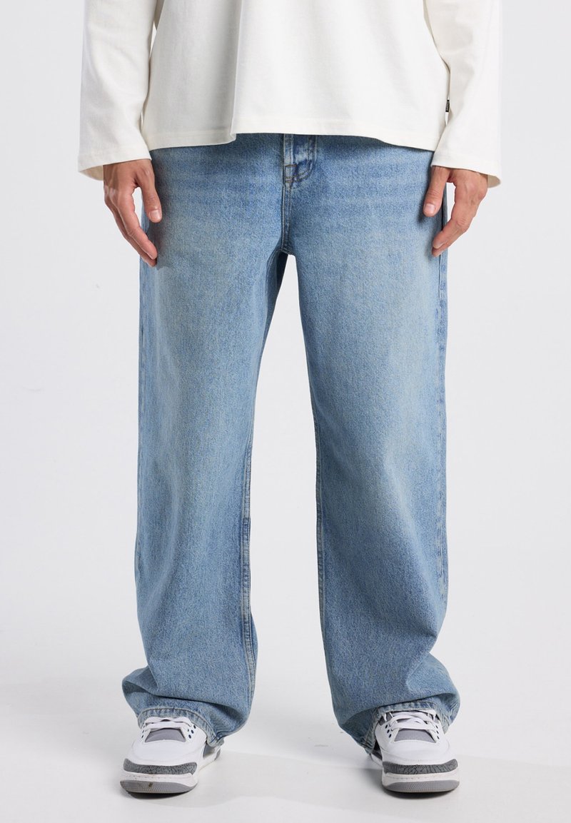 Lichtblauwe denim jeans met een relaxte pasvorm, voorzien van vijf zakken en subtiele vervaging. Gecombineerd met witte sneakers voor een casual uitstraling.