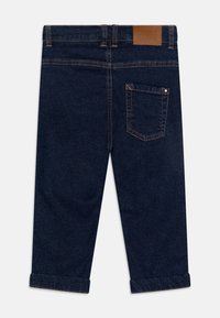 Tummansininen farkkusukka suoralla lahkeella, käännetyillä reunuksilla, kontrastivärillä ommeltuna ja nahkalaastari takavyötäröllä.