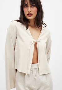 Cremefarvet cropped top med V-hals og bindeb�ånd foran, med løse ærmer og struktureret stof. Sammen med matchende underdel.