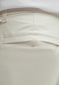 Beige broek met een gladde textuur, voorzien van een achterzak met knoopsluiting en een ceintuurlus in de taille.