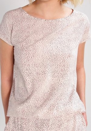 Nærbillede af en person iført en lyserød kortærmet top med små sorte prikker og matchende underdel.