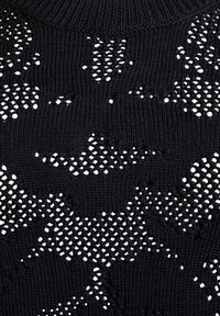 Pull en tricot noir avec un motif texturé et des mailles ouvertes, créant un intérêt visuel grâce au contraste entre la matière solide et l'espace négatif.