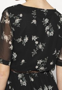 Musta mekko, jossa on vaaleanpunaisia ja vihreitä kukkakuoseja. Lyhyet läpinäkyvät hihat ja ruskea vyö vyötäröllä. Saumaton, kevyestä kankaasta valmistettu.