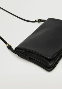 Borsa a tracolla in pelle nera con texture liscia, design pieghevole e dettagli in oro. Tracolla regolabile per una maggiore versatilità.