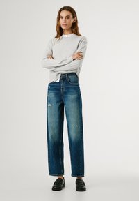 Světle šedý svetr, modré široké džíny s distressed detaily a černé boty. Neformální outfit s vrstveným vzhledem, který zahrnuje límeček košile.