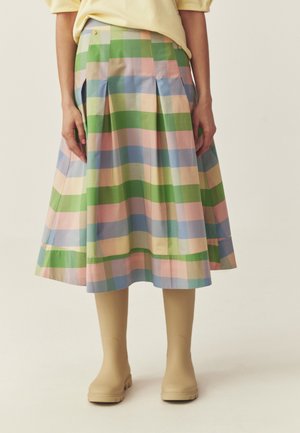Sukňa so záhybmi po kolená s károvaným vzorom v pastelovej zelenej, ružovej, modrej a žltej farbe, nosená s béžovými členkovými topánkami.