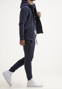 Námořnická mikina na zip a odpovídající tepláky z měkké látky, s předními kapsami a žebrovanými manžetami, doplněné bílými teniskami.