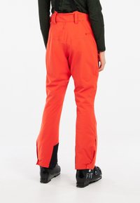 Pantalons imperméables rouges avec des accents noirs, bretelles ajustables et coupe aérodynamique. Caractéristiques zips latéraux aux chevilles et coutures renforcées.