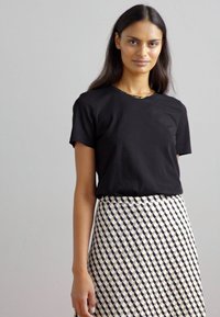 Zwart T-shirt met korte mouwen, gecombineerd met een gemêleerde rok met een geometrisch ontwerp in crème en marineblauw. Glad materiaal met een getailleerde snit.