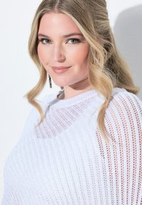 Biały sweter z dzianiny o luźnym kroju, z poziomymi paskami i teksturowanym wykończeniem. Podkreślony okrągłym dekoltem i przezroczystymi detalami.