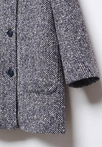 Navy and white textured wool coat with black buttons and front pockets, shown hanging against a white background.