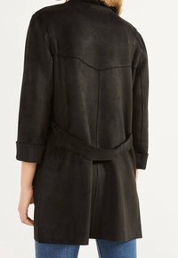 Giacca in suede nero con vestibilità rilassata, vita regolabile con cintura e polsini arrotolati. Caratterizzata da una texture liscia e un design con yoke posteriore.