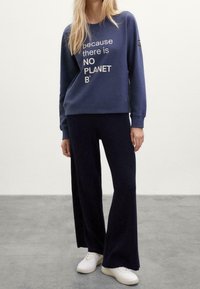 Sudadera azul marino con texto blanco que dice "porque NO HAY UN PLANETA B", combinada con pantalones de pierna ancha de canalé a juego y zapatillas blancas.