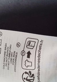 Care instructions displayed on a textured, white fabric label. Symbols indicate washing, drying, and ironing guidelines.